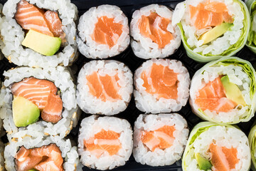 Top view of a takeaway tray of salmon makis of various types. Oriental, Japanese food. Takeaway. Shot with macro lens.