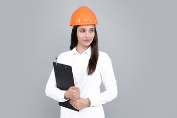 Young woman construction manager. Woman builder isolated portrait with protect helmet and clipboard. Gray background, copy space.