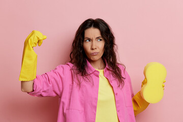 Strong and independent housewife shows muscle with serious look, isolated over pink wall