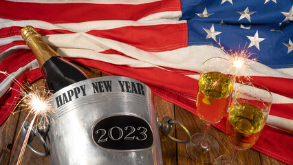 New Year 2023 New Year's Eve Sylvester holiday celebration background USA greeting card - American flag, sparkling wine or champagnebucket, bottle and glasses and sparklers on wooden table, top view
