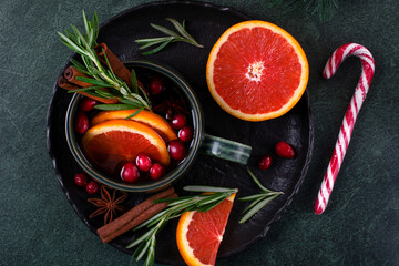 Mulled wine served with red orange, cinnamon, cranberry and rosemary in green ceramic mug on dark table. Christmas and winter warming drink. Top view