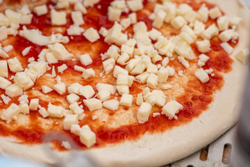 Hand with plastic glove preparing pizza with tomato sauce, fresh mozzarella, mushrooms and green basil leaves on a wooden board, close up