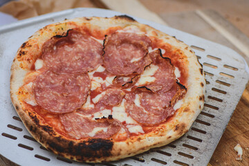 Serving hot pizza with tomato sauce, mozzarella cheese and salami meat with a shovel on a wooden board, close up