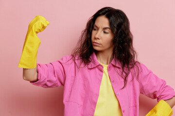 Young independent brunette housewife, shows a muscle and power, isolated over pink wall