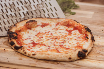 Serving hot pizza Margherita with tomato sauce and mozzarella cheese with a shovel on a wooden board, with smoke