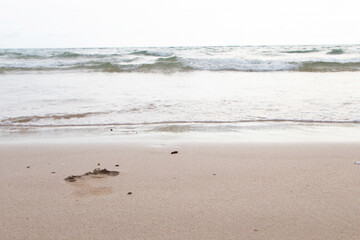Beautiful wave soft blue ocean wave on clean sandy beach.with footprints on brown sand. Summer day and sandy beach background concept. Waves sea crashing shore texture Background. Close up no people.