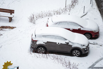 City street driveway parking lot spot with small car covered snow stuck trapped after heavy blizzard snowfall winter day by big snowy pile. Snowdrifts and freezed vehicles. Extreme weather conditions.