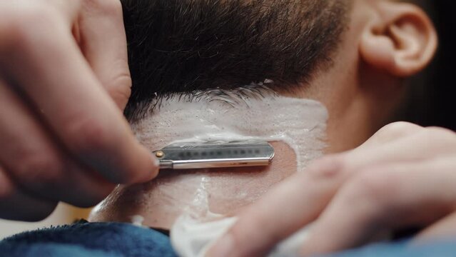 Close-up barber shaves client's beard with a straight razor and foam. Barber shaving, outlining beard, providing service for a barbershop salon visitor