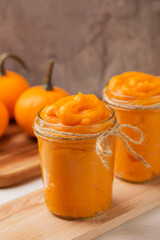 Homemade organic pumpkin puree in glass jars and mini pumpkins on dark background close up. Ingredient for autumn or winter recipes. Seasonal cooking concept. Fall time. Vertical orientation.