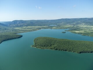 Aerial view on mountain lake. Drone over water reservoir at mountain valley covered with green spring forest. Beautiful view from above on smooth blue surface of mountain lake among highlands. Nobody