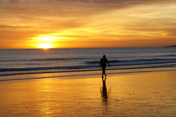 Un homme se promène sur une plage de l'Algarve au Portugal au coucher du soleil