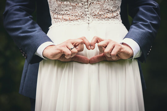 a bride and groom with wedding rings form a heart