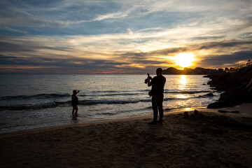 La silueta de un hombre haci&eacute;ndole una foto a su pareja en la playa de Benidorm con el precioso cielo al atardecer de fondo en un d&iacute;a de oto&ntilde;o.