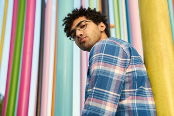 Low angle of the pensive middle eastern man wearing eyeglasses looking at the camera standing near the colorful wall. Human lifestyle concept 