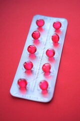 Red round capsules in a blister pack on a red table