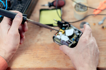 A man collects radio components. He puts it on the board and soldering it with a soldering iron. Assembly of the electrical part of the device by human hands. Electrical parts. Solder with tin.