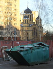 Fototapeta na wymiar Green metal dumpster in the yard next to the church, Kollontai Street, St. Petersburg, Russia, December 2022