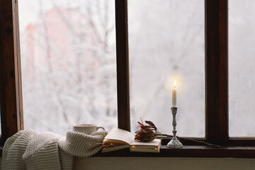 Cozy winter still life. Cup of hot tea and an open book with a warm sweater on a vintage wooden windowsill. Cozy home concept. Sweet home.