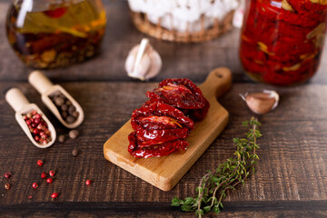 Sun-dried tomatoes in olive oil on a mini board with pepper, garlic and thyme in a rustic style. Selective focus, close-up.