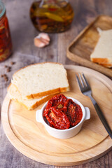 Sun-dried tomatoes in olive oil on a round board with homemade bread in a rustic style. Traditional home cooking. Selective focus, close-up.