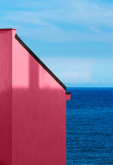 Viva magenta wall of building with a sea and sky background. Minimal abstract concept. Color trend year 2023.