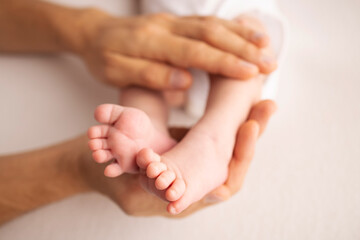 Obraz na płótnie Canvas Children's foot in the hands of mother, father, parents. Feet of a tiny newborn close up. Little baby legs. Mom and her child. Happy family concept. Beautiful concept image of motherhood stock photo. 