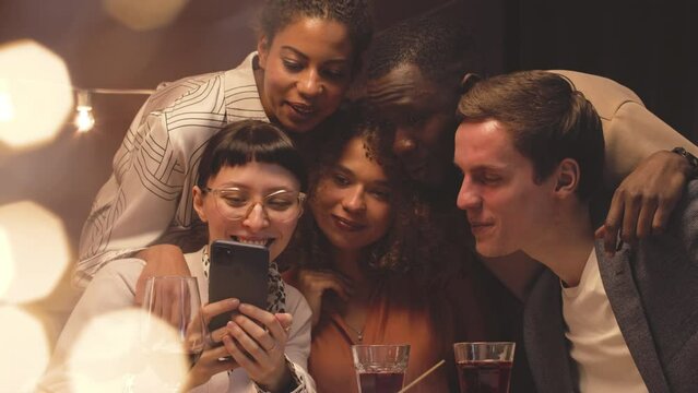 Company of young cheerful diverse friends taking funny selfies on smartphone camera during festive dinner party on Christmas