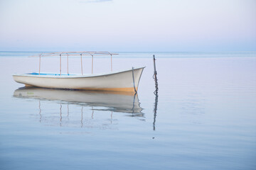 Une pirogue en bois de pêcheurs, sur un lagon calme à la lumière du petit matin exprimant douceur et sérénité.