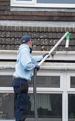 A window and gutter cleaner cleaning Dirty clogged white plastic pvc gutters and drain pipes with...