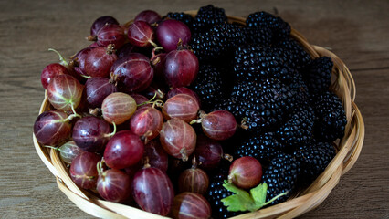 Ripe, juicy gooseberries and blackberries in a wicker plate.