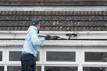 A window and gutter cleaner cleaning Dirty clogged white plastic pvc gutters and drain pipes with...