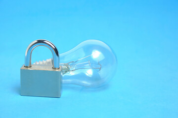 Incandescent lamp and lock on blue background.Concept of power outage.