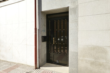 Small metal door to the street painted black and gold handles in a detached house building with a gray granite facade