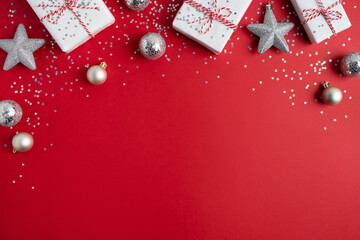 Christmas presents, silver confetti, various ornaments on red background. Gifts wrapped in white...