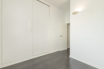 Empty room in a house with a gray laminated wooden floor, white painted plain walls and white lacquered wooden sliding doors