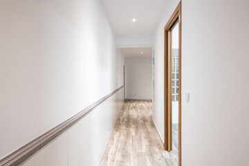Long corridor of a house with a stoneware floor similar to wood and a wall with a skylight
