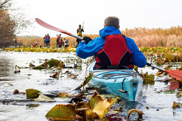 Rear view of people paddle in blue kayak and stand up paddle boards in river among the autumn water lilies