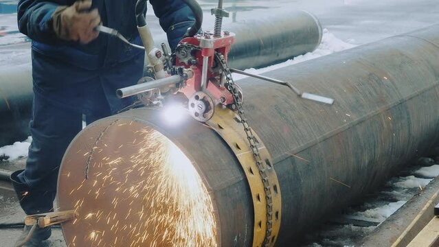 Welder cuts large diameter metal pipe and sparks fly. Industrial pipe cutting device. Stabilized video. Authentic workflow..