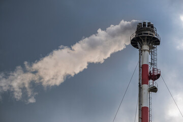 Smokestack exhaling smoke in a refinery with the sky in the background