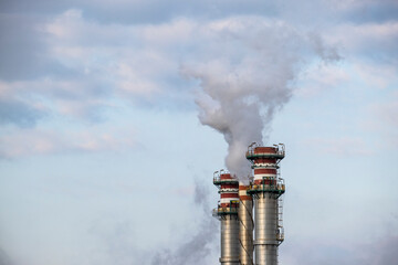 Smokestack exhaling smoke in a refinery with the sky in the background