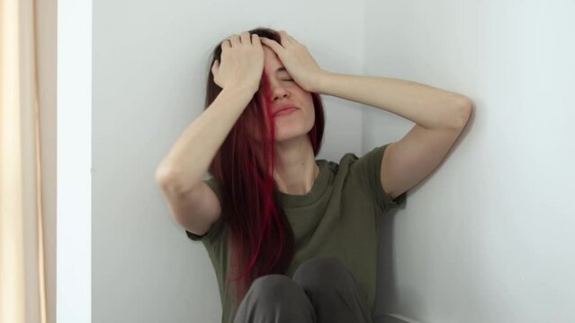 Nervous woman suffering from depression, sitting alone at home in a corner and holding her head, PTSD concept.