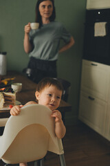 portrait of mom and child at home looking out for dad mom drinking tea baby sitting behind a high chair