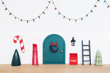 Mini elf or mouse house diy toy gift for kids made with tiny door, mail box, red ski, lantern, Christmas green tree and wreath. Little bulb garland on white wall. Holiday decor idea with copy space.