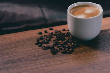White cup of coffee with sunlight in morning and coffee beans on wooden table and black...