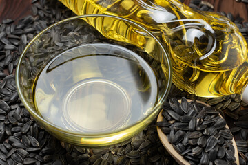 Sunflower oil in glass bowl and bottle with seed in wooden spoon on wooden background