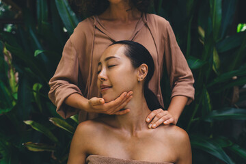 Cropped female cosmetologist doing face massage during dayspa with client on nature, Asian woman...