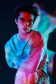 Young man in straitjacket standing against neon illumination