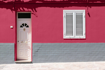 White wooden front door and white window on magenta brick wall. Color trend of the year 2023