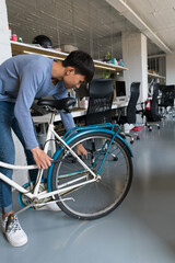Young Asian man fixing bicycle in office building.