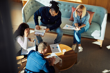 Diverse businesspeople smiling while discussing charts in an office lounge